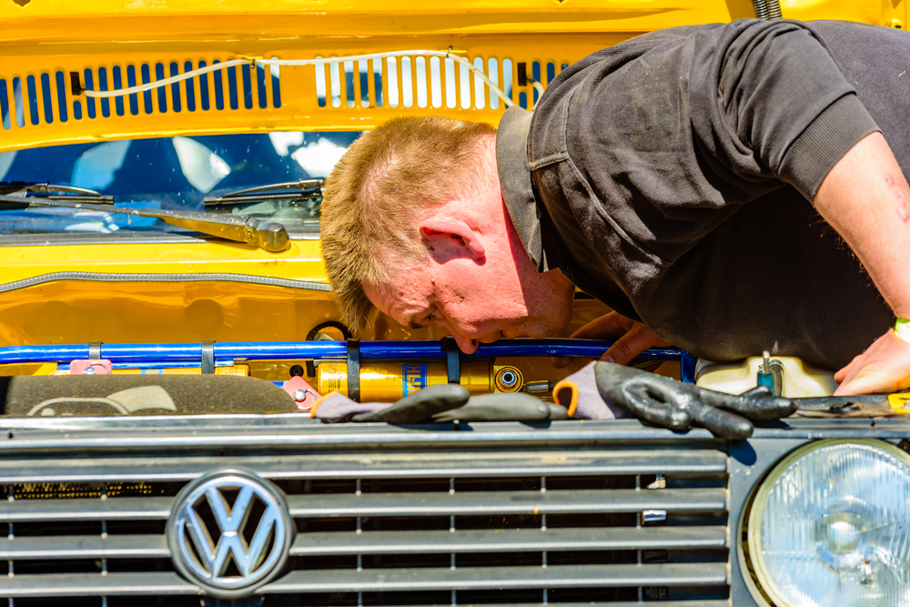 Mechanic bent over looking under the bonnet of a Volkswagen according to recommended maintenance schedule.